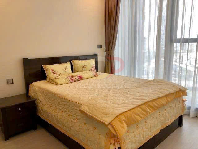 Giường ngủ gỗ với chăn ga gối màu vàng hoa văn trong phòng ngủ sáng có cửa kính lớn