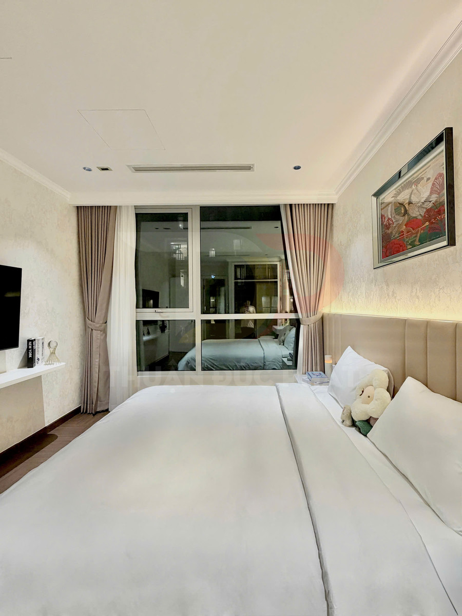 Phòng ngủ hiện đại với giường đôi trải ga trắng, gối ôm hình thú, cửa kính lớn và rèm màu be