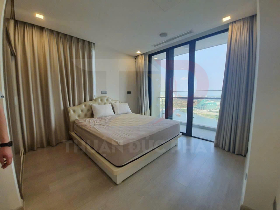 Phòng ngủ hiện đại với giường đôi bọc da màu kem cạnh cửa kính lớn nhìn ra ban công và view biển