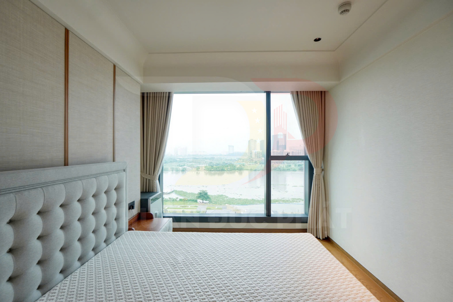 Phòng ngủ căn hộ với giường bọc nệm sáng màu và cửa sổ lớn nhìn ra sông và thành phố