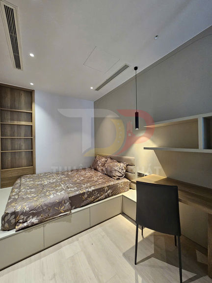 Phòng ngủ hiện đại với giường bọc nệm hoa văn nâu, tủ kệ gỗ và bàn làm việc liền kệ gọn gàng