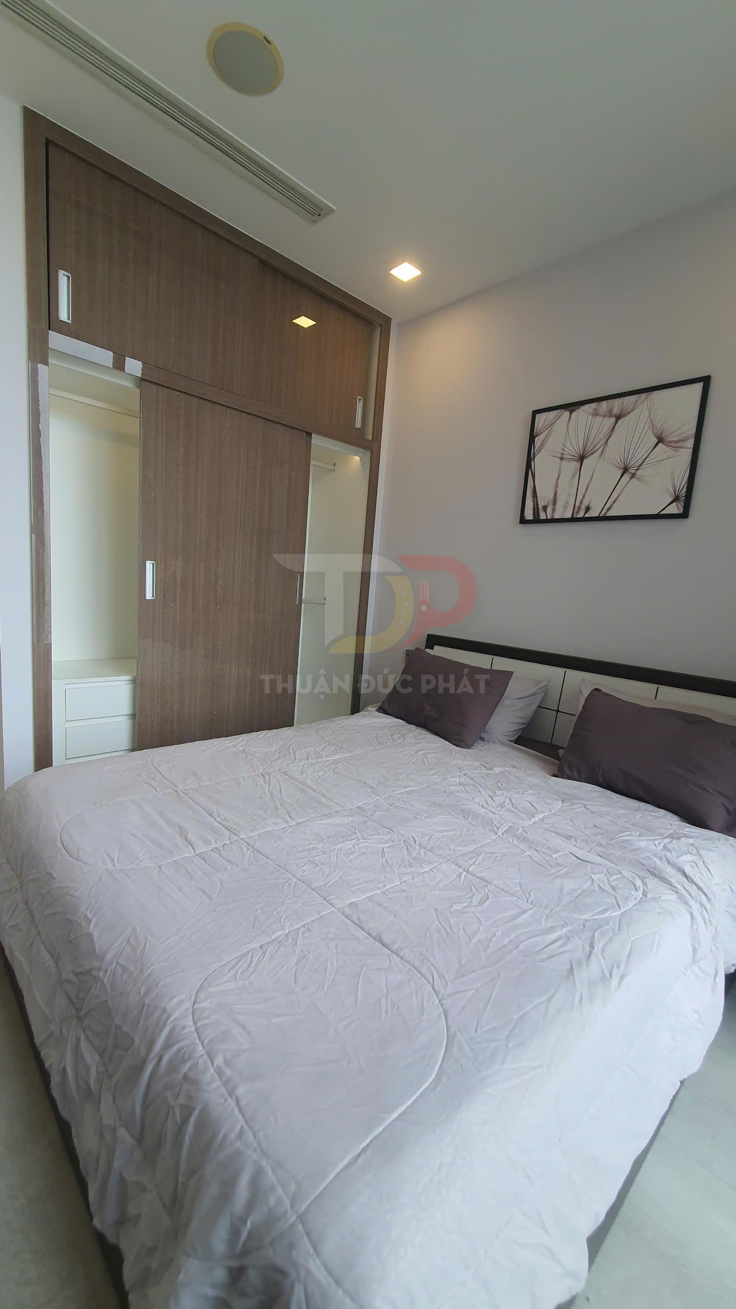 Phòng ngủ hiện đại với giường đôi ga trải màu sáng, tủ quần áo gỗ cửa lùa và tranh treo tường trang trí