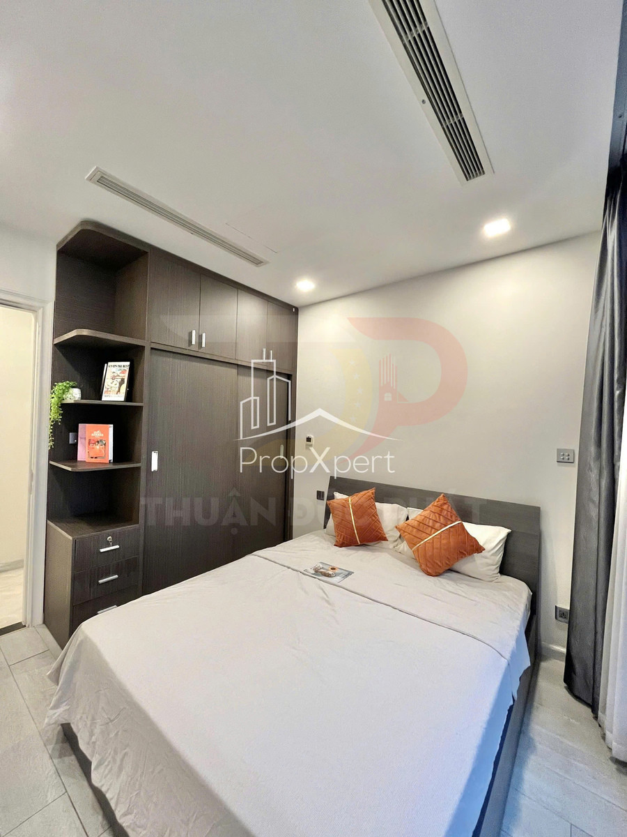 Phòng ngủ hiện đại với giường đôi ga màu sáng, gối tựa cam và tủ quần áo gỗ âm tường