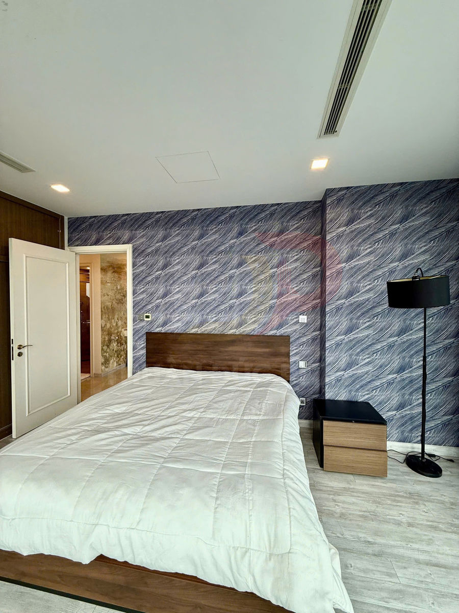 Giường ngủ gỗ với chăn trắng, cạnh bàn đầu giường và đèn sàn trong phòng ngủ hiện đại tường họa tiết xanh