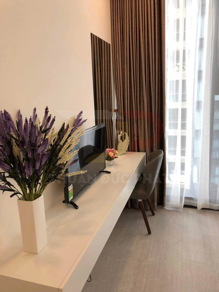 Bàn làm việc gắn tường màu trắng với tivi phẳng, ghế nệm và bình hoa trang trí cạnh cửa sổ có rèm dài
