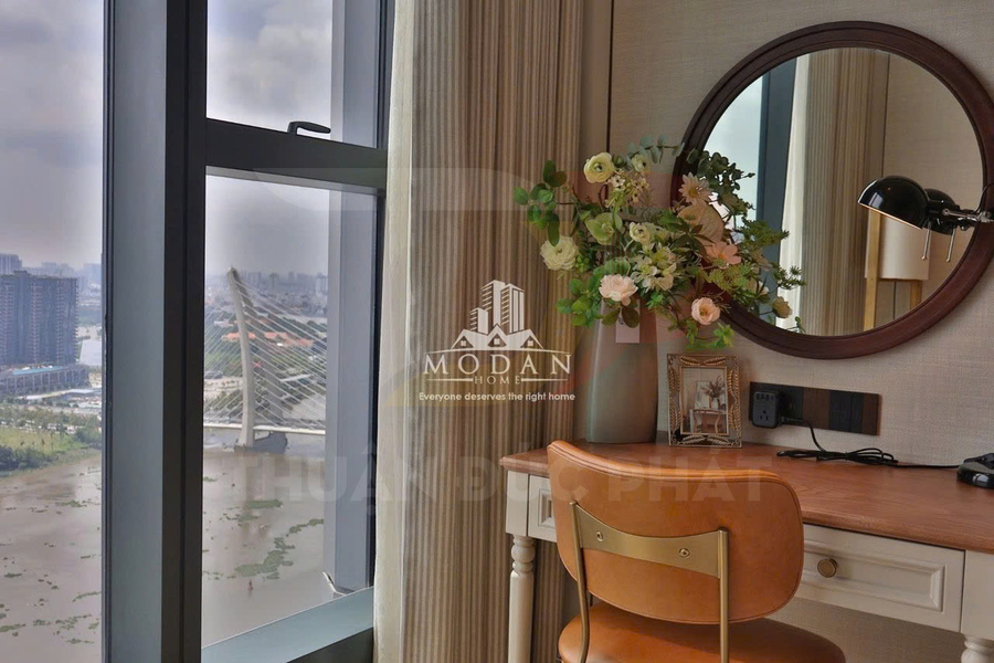 Bàn làm việc gỗ cạnh cửa sổ view sông với ghế da nâu, gương tròn và bình hoa trang trí