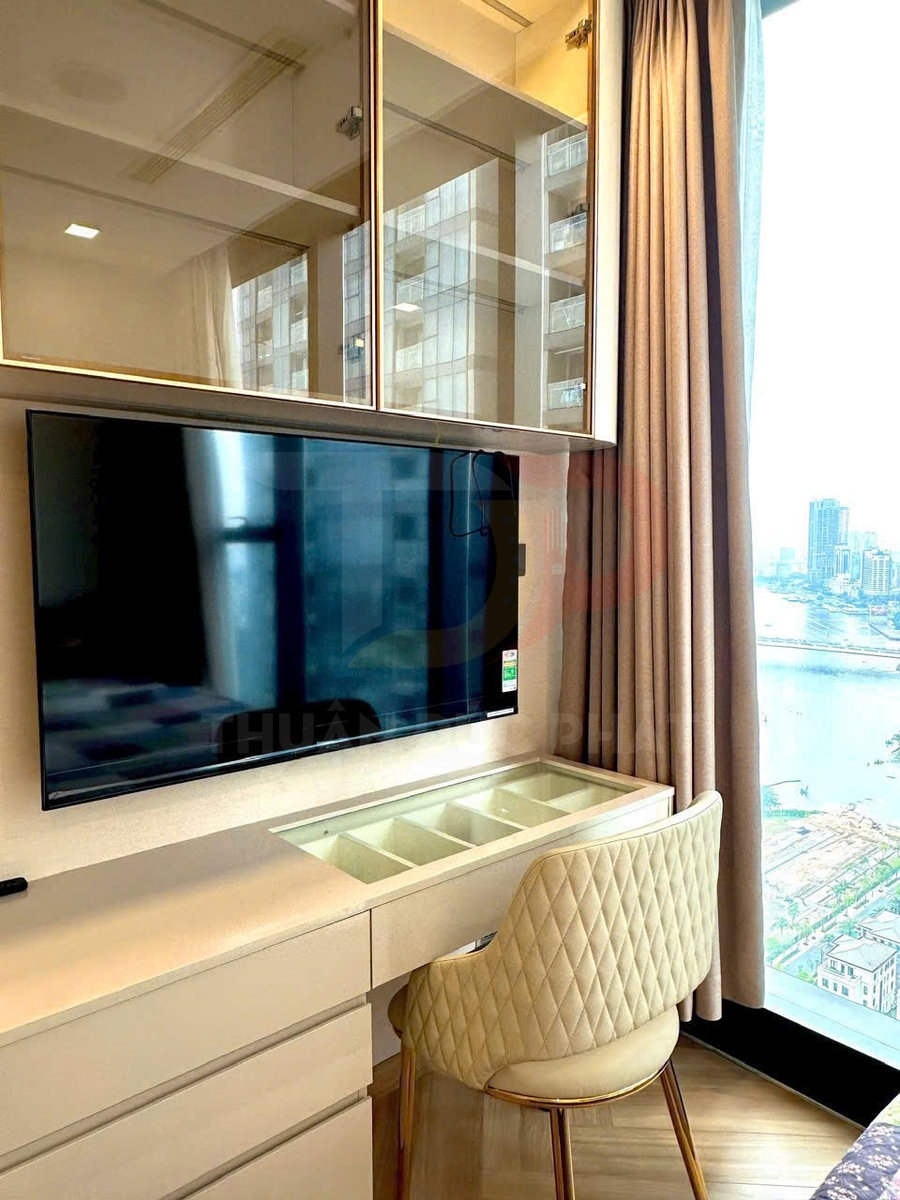 Bàn làm việc gỗ có ngăn kéo, ghế nệm lưng caro và tivi treo tường cạnh cửa sổ lớn view thành phố