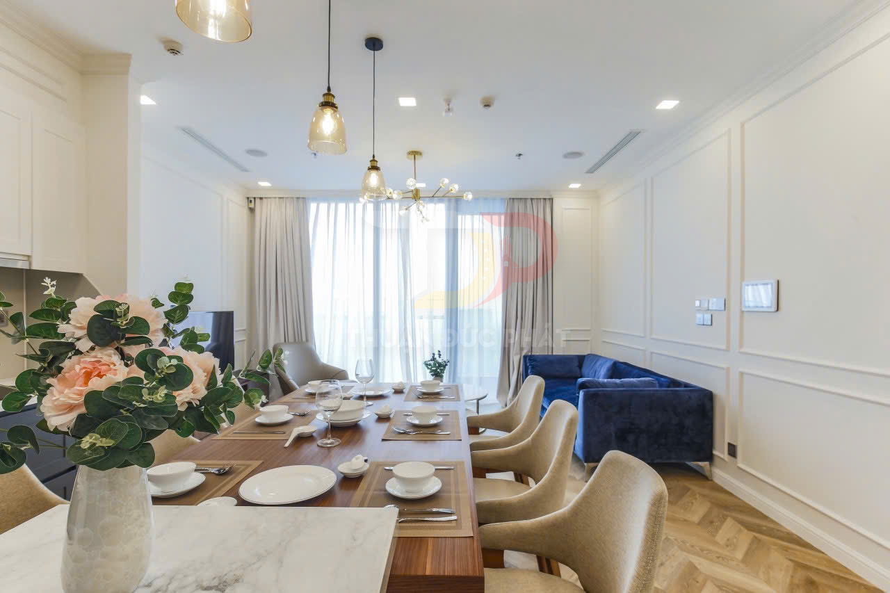Phòng ăn chung cư cao cấp với bàn gỗ bày biện bát đĩa sang trọng và sofa xanh trong phòng khách