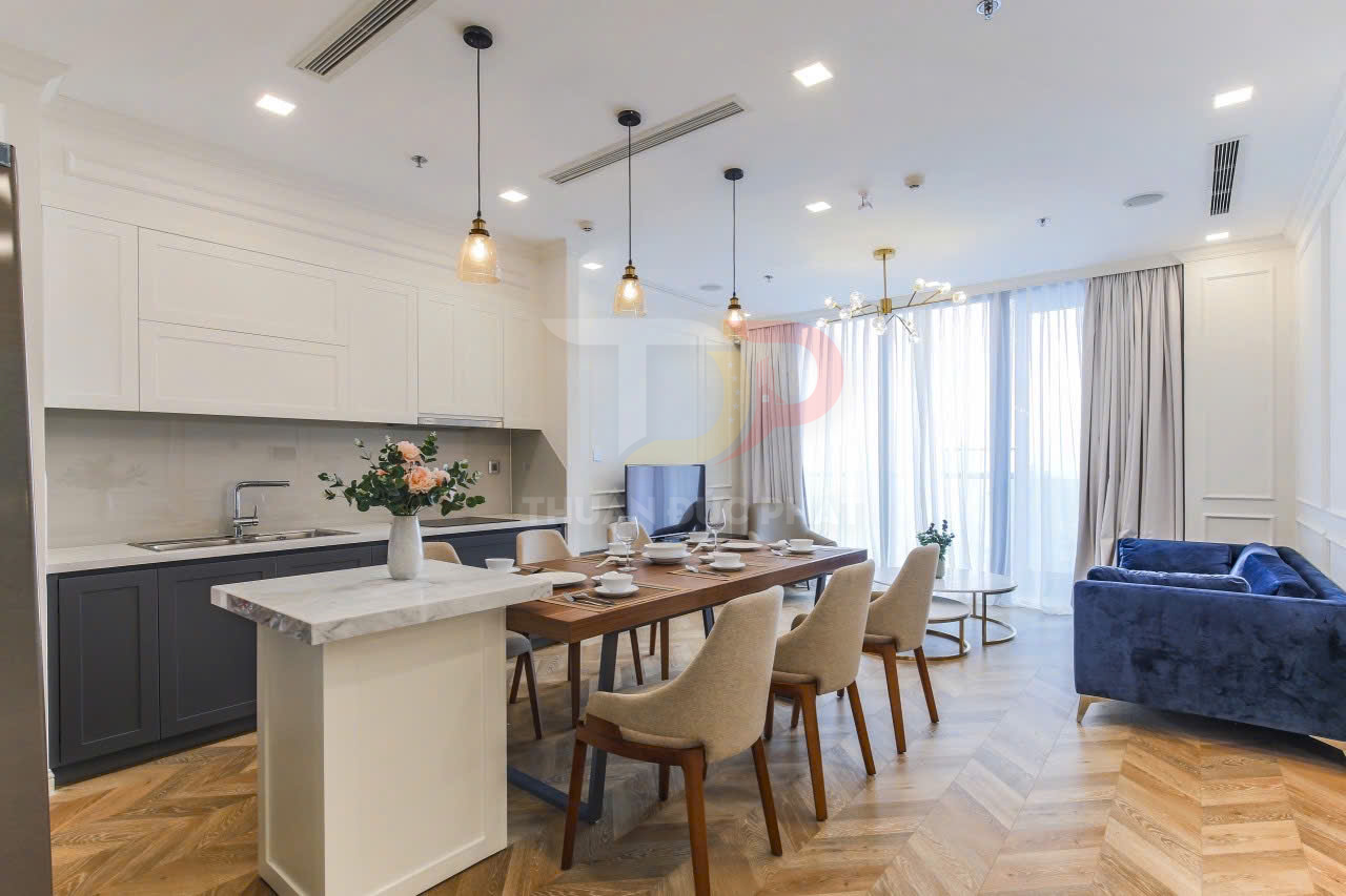 Phòng bếp và phòng khách chung cư hiện đại với bàn ăn gỗ, ghế nệm và sofa xanh sang trọng