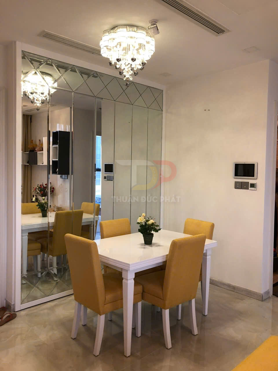 Bộ bàn ăn gỗ màu trắng bốn ghế bọc nệm vàng đặt cạnh tường gương trong phòng ăn hiện đại