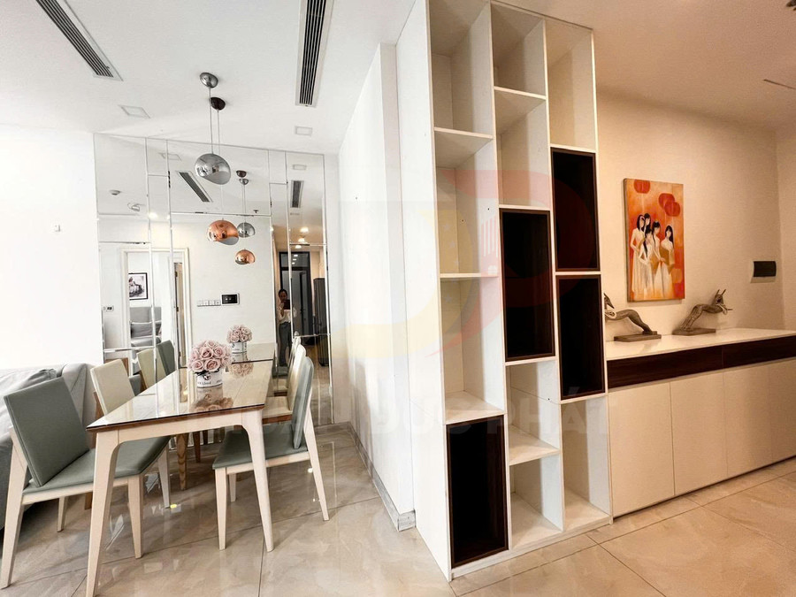 Bàn ăn gỗ hiện đại với ghế bọc nệm cạnh kệ tủ trang trí trắng trong phòng ăn chung cư sáng sủa