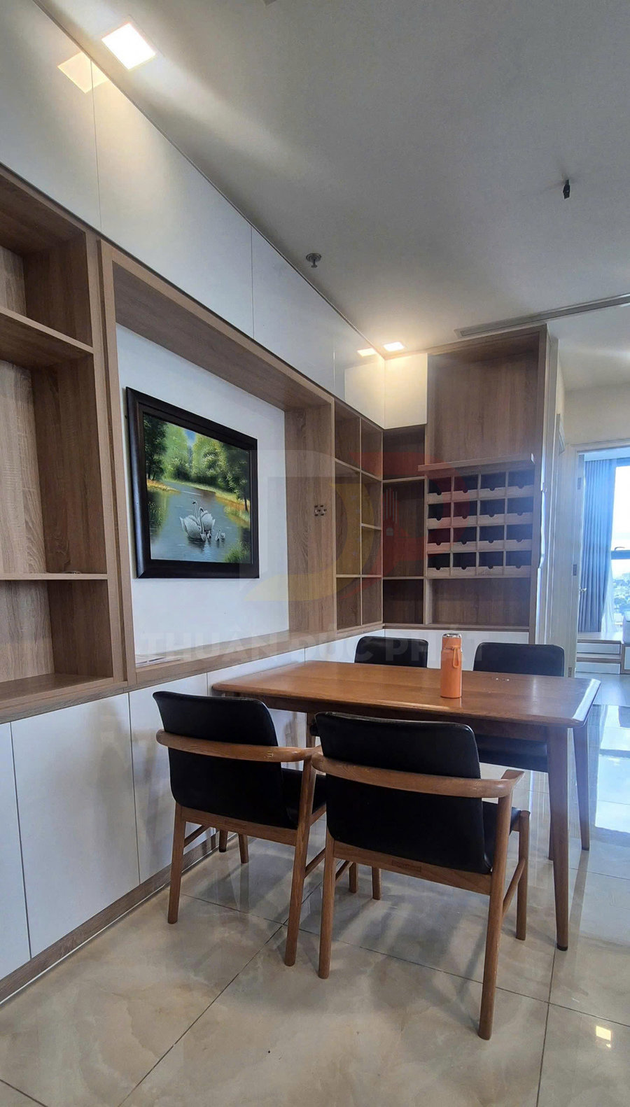 Bộ bàn ghế gỗ phòng ăn hiện đại với hai ghế tựa bọc nệm đen và tủ kệ gỗ âm tường phía sau