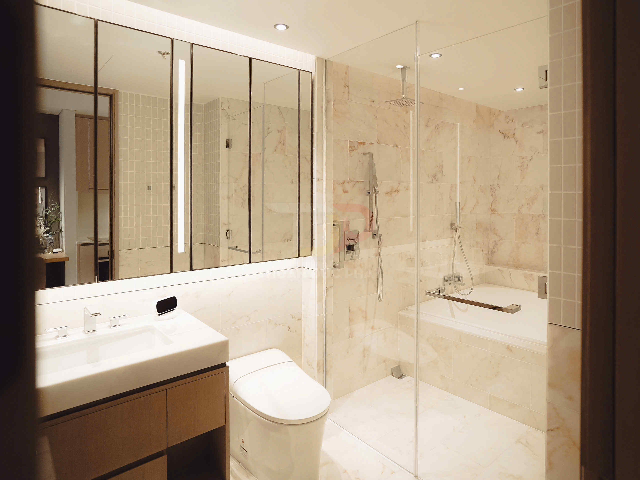 Phòng tắm hiện đại với bồn tắm kính, vòi sen âm trần, bồn cầu và lavabo đá màu kem