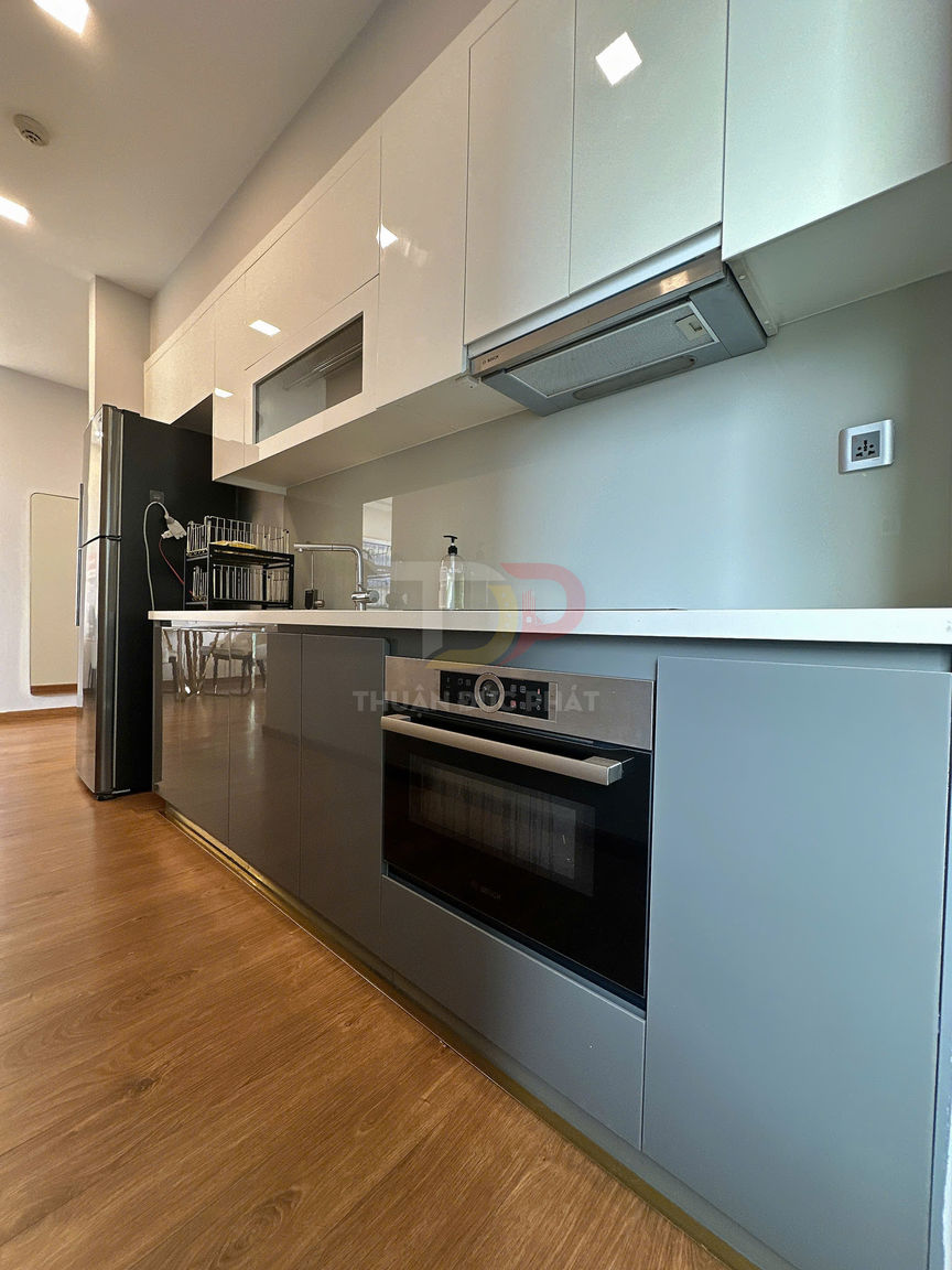 Tủ bếp hiện đại màu trắng xám với lò nướng âm tủ, bếp từ và máy hút mùi trên nền sàn gỗ