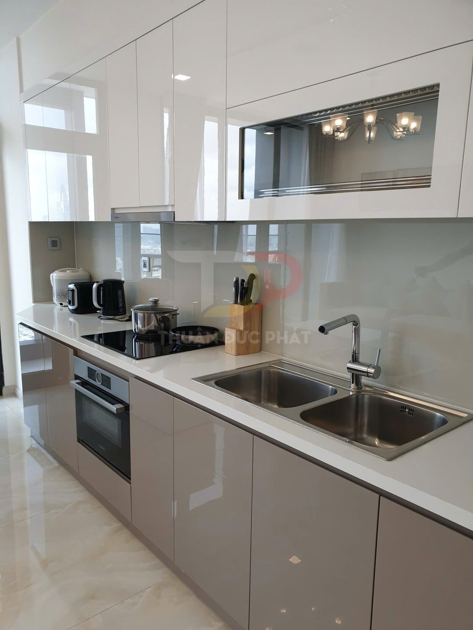 Tủ bếp hiện đại màu trắng kem với bếp từ, lò nướng âm tủ và chậu rửa đôi inox trong căn hộ cao cấp