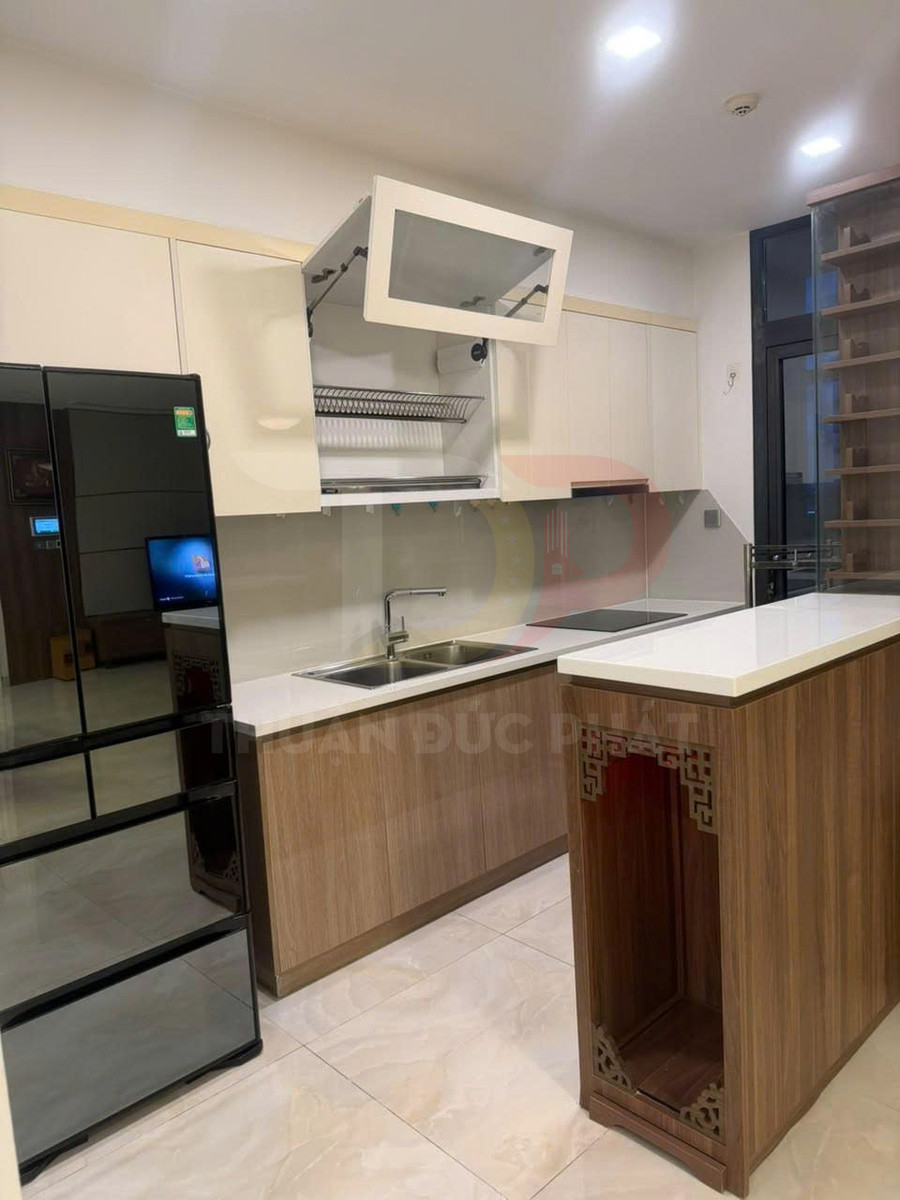 Tủ bếp gỗ hiện đại với kệ úp chén nâng hạ, đảo bếp mặt đá và tủ lạnh kính đen sang trọng