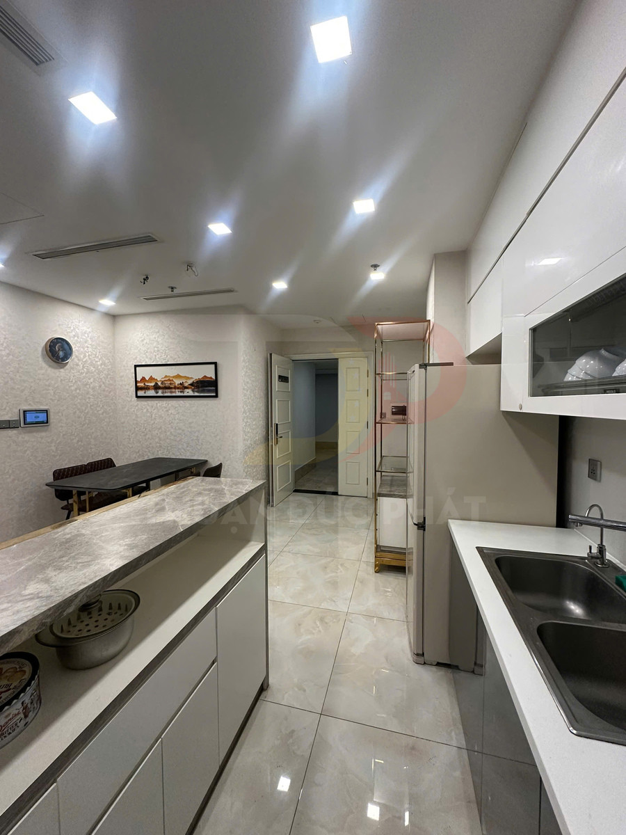 Gian bếp hiện đại với tủ bếp trắng, mặt đá, bồn rửa đôi và bàn ăn nhỏ phía sau