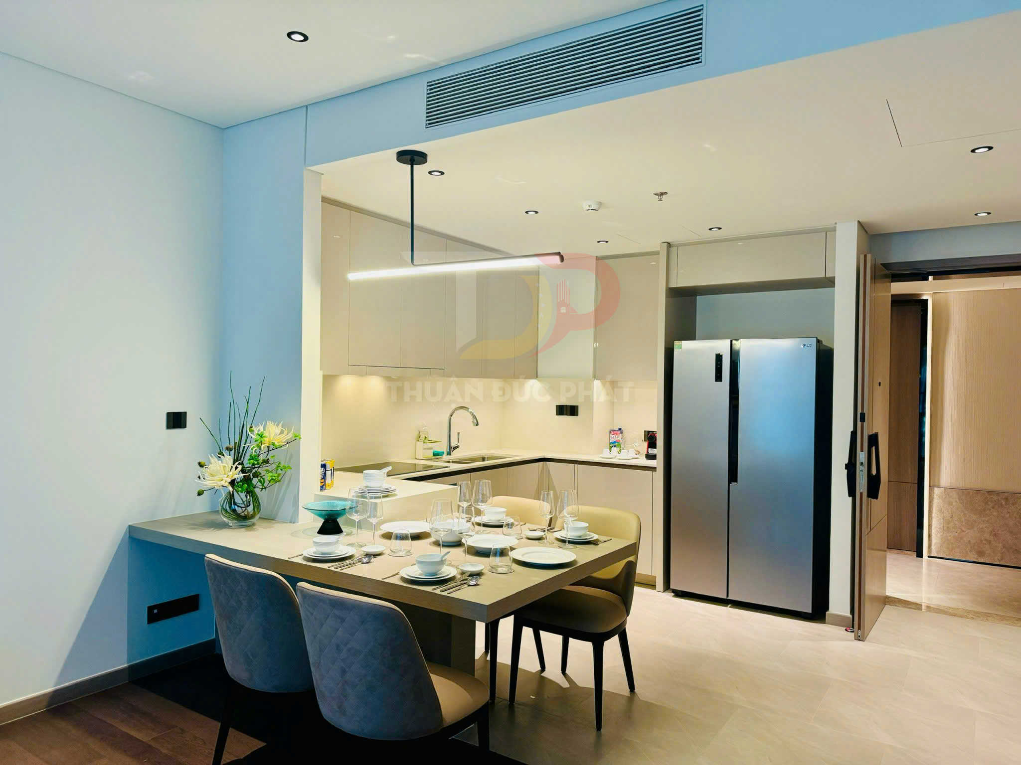 Bộ bàn ăn hiện đại bày biện sẵn cạnh bếp và tủ lạnh đôi inox trong căn hộ cao cấp
