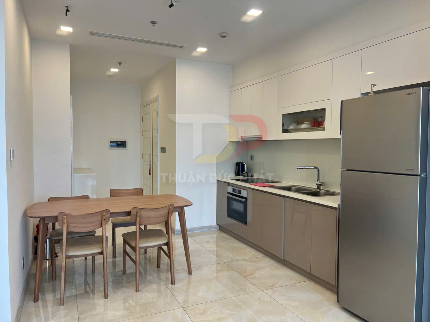 Bếp hiện đại với tủ bếp trắng, bàn ăn gỗ bốn ghế và tủ lạnh Hitachi inox trong căn hộ sáng sủa