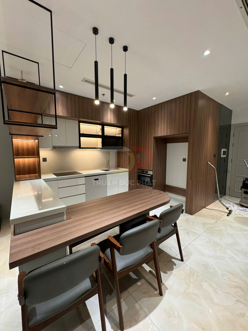 Bếp hiện đại với tủ gỗ, bàn đảo kết hợp bàn ăn gỗ và ba ghế, đèn thả trần tối giản