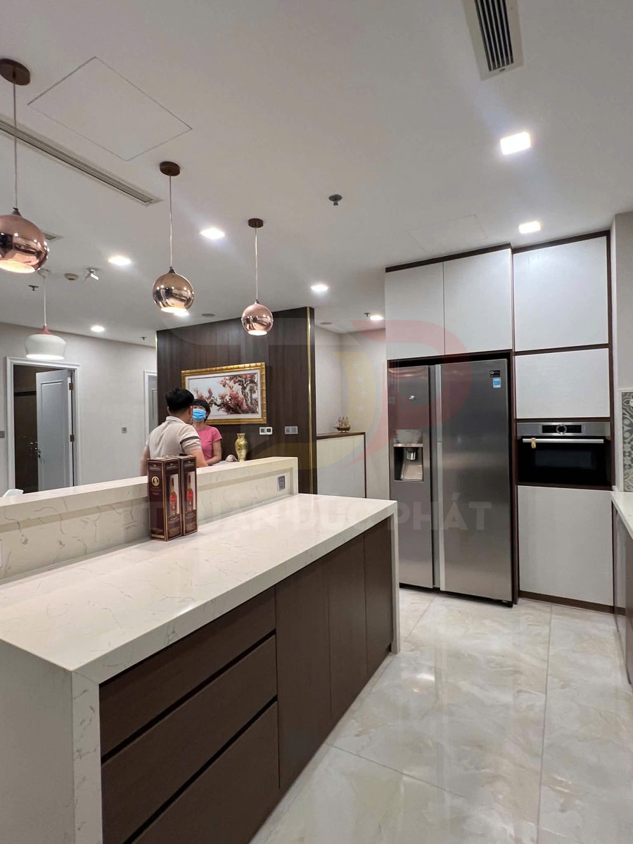 Bếp hiện đại với tủ gỗ, đảo bếp mặt đá trắng và tủ lạnh đôi inox có máy làm đá