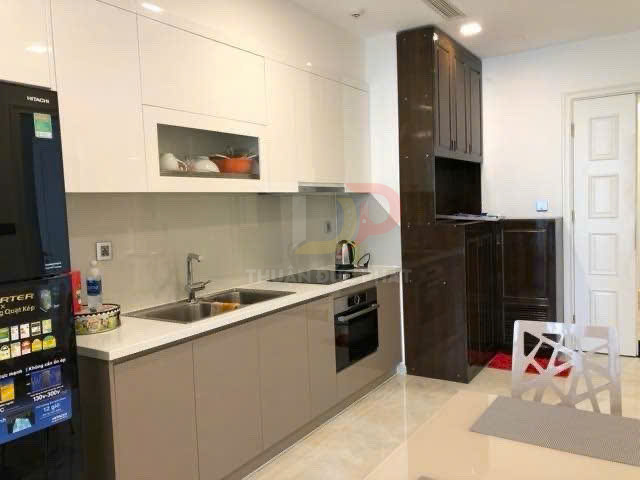 Gian bếp hiện đại với tủ bếp gỗ, bồn rửa inox, bếp âm tủ và tủ lạnh lớn màu đen