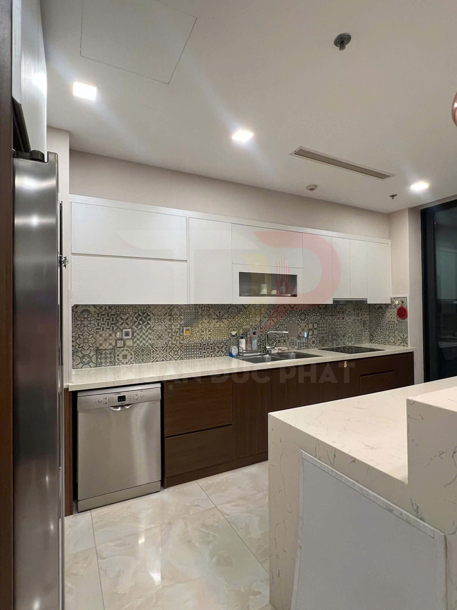 Tủ bếp gỗ hiện đại với mặt đá trắng, máy rửa bát inox và bồn rửa đôi trong không gian bếp sáng sạch
