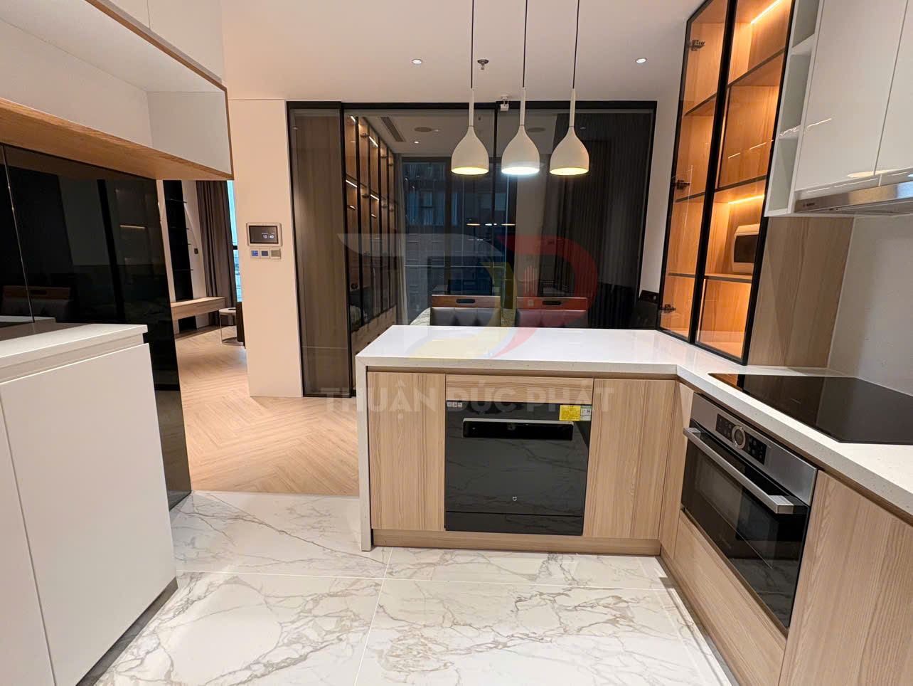 Tủ bếp chữ U hiện đại với mặt đá trắng, tủ gỗ sáng màu và bếp âm tủ trong căn hộ cao cấp