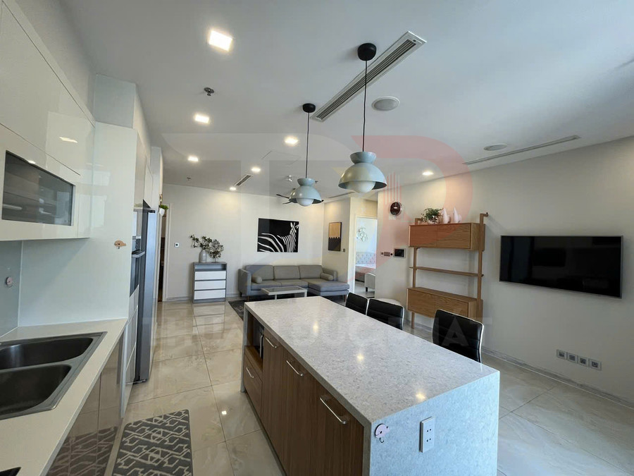 Căn hộ hiện đại với bếp đảo mặt đá, tủ bếp trắng, sofa xám và tivi treo tường trong không gian mở sáng sủa