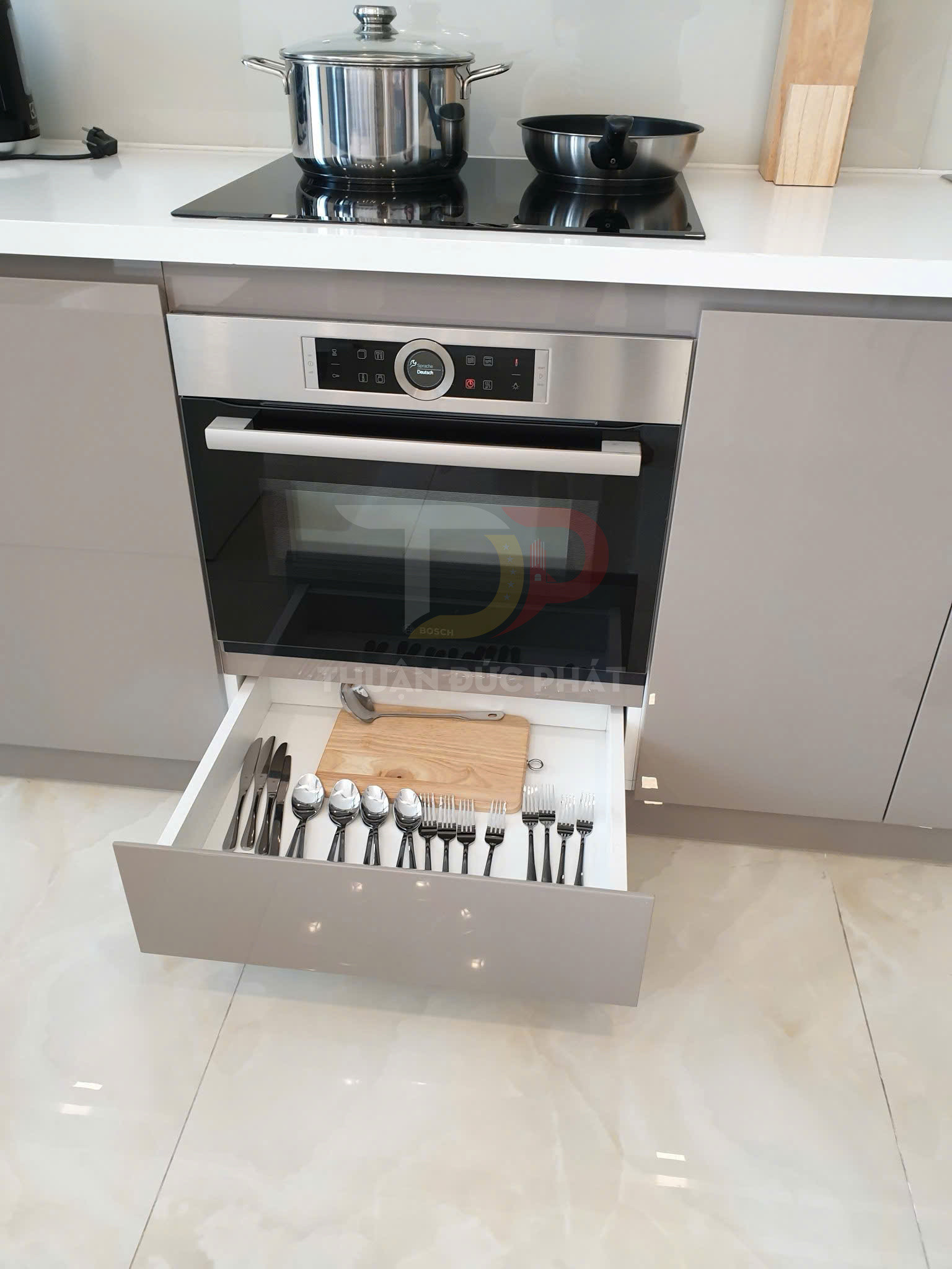 Ngăn kéo bếp âm tủ gọn gàng với khay đựng muỗng nĩa và thớt dưới bếp từ và lò nướng Bosch
