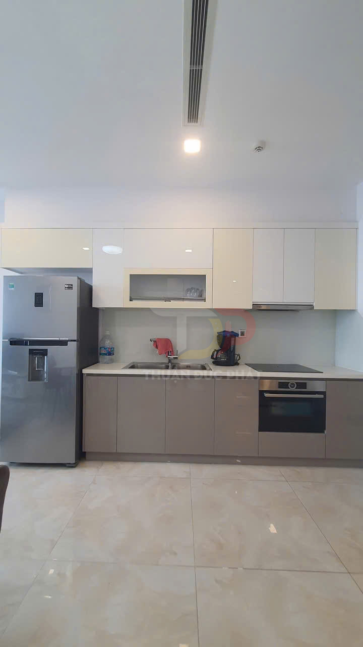 Tủ bếp hiện đại kèm bếp điện âm, lò nướng và tủ lạnh inox trong không gian bếp chung cư sáng sủa