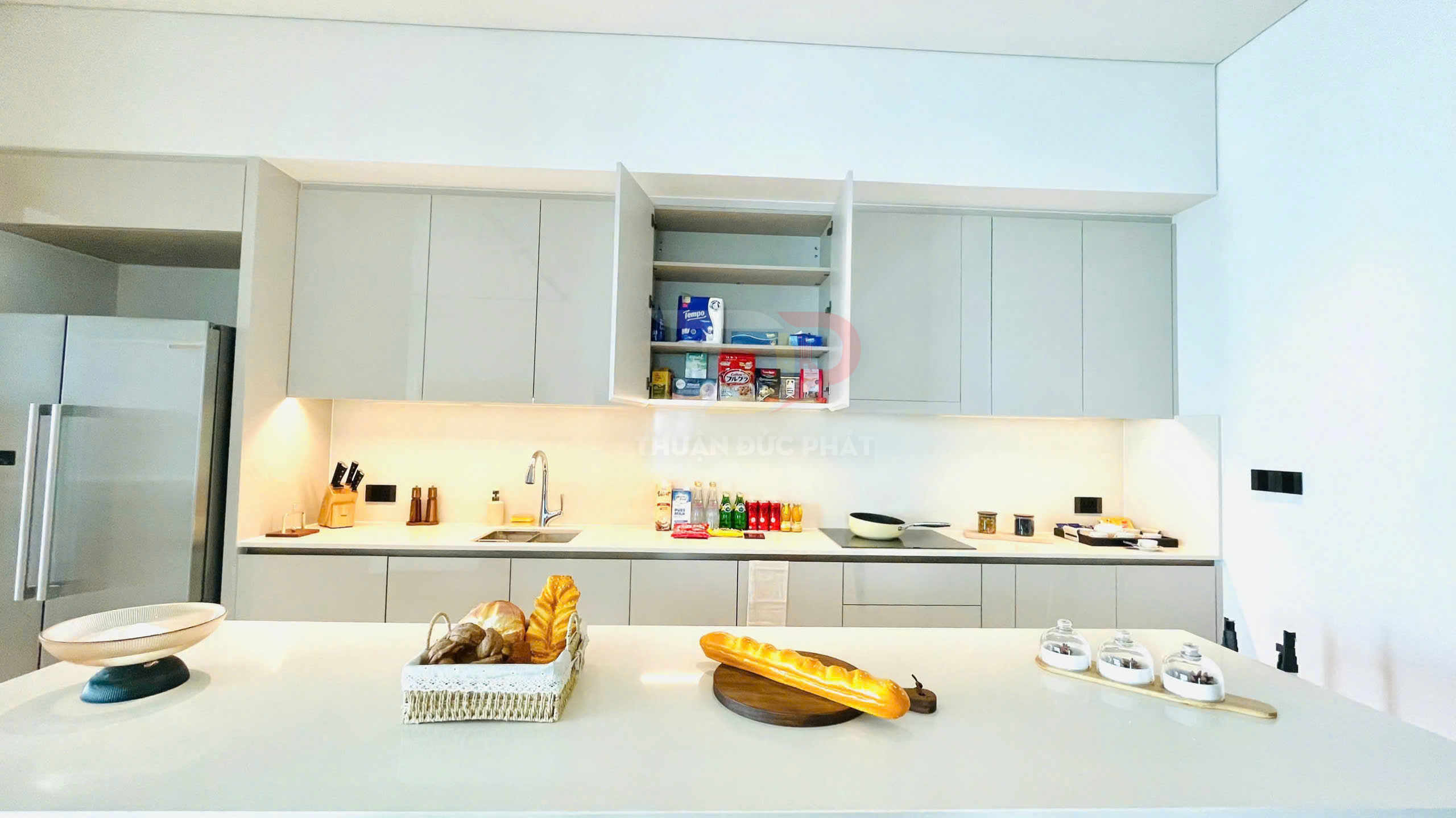 Bếp hiện đại với tủ bếp màu trắng, đảo bếp bày bánh mì và đồ gia dụng gọn gàng