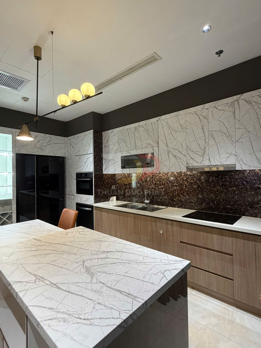 Bếp hiện đại với tủ gỗ, đảo bếp đá vân mây, bếp từ âm và tủ lạnh âm tường màu đen