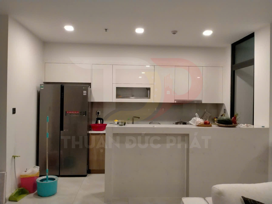 Tủ bếp chữ I hiện đại màu trắng với tủ lạnh LG inox và quầy bar nhỏ trong căn hộ