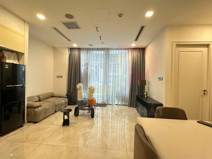 Phòng khách căn hộ hiện đại với sofa da, bàn trà nhỏ, tủ lạnh đen và cửa kính lớn có rèm xám