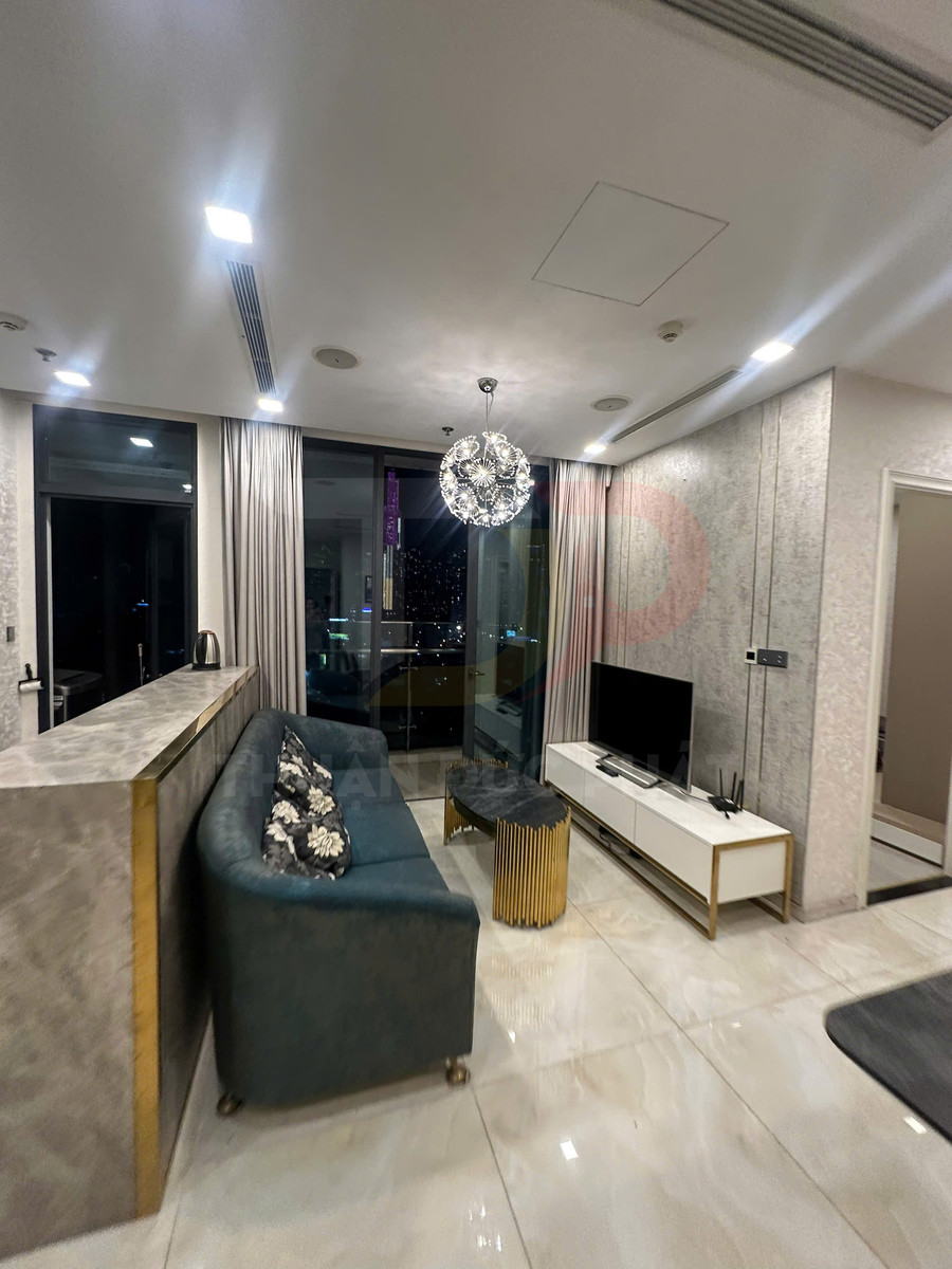 Phòng khách chung cư hiện đại với sofa xanh, bàn trà vàng, kệ tivi trắng và cửa kính nhìn ra thành phố ban đêm