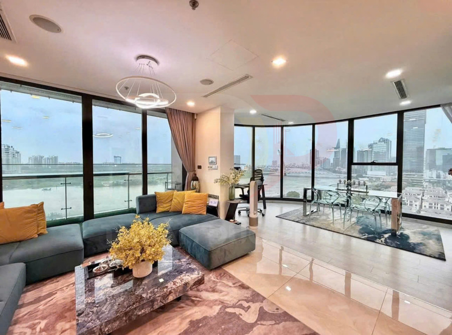 Phòng khách căn hộ cao cấp với sofa chữ L, bàn đá và cửa kính lớn nhìn ra sông và skyline thành phố