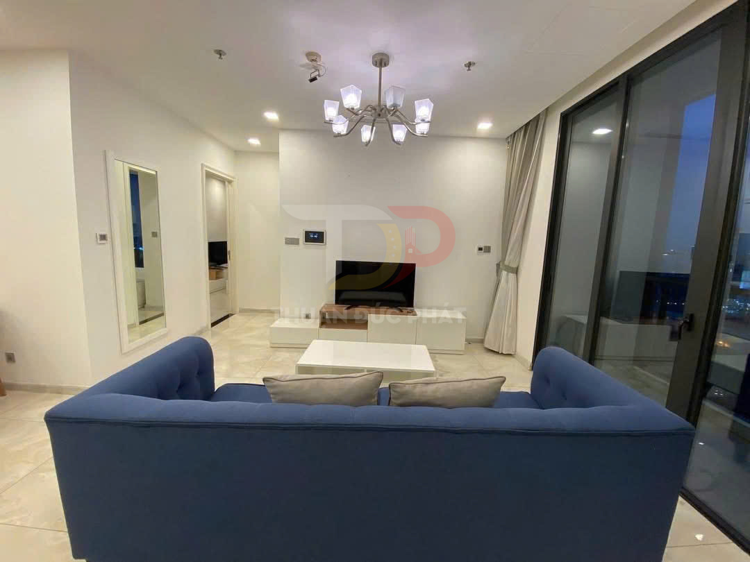 Phòng khách chung cư hiện đại với sofa xanh, bàn trà trắng, tivi treo tường và cửa kính lớn nhìn ra ban công