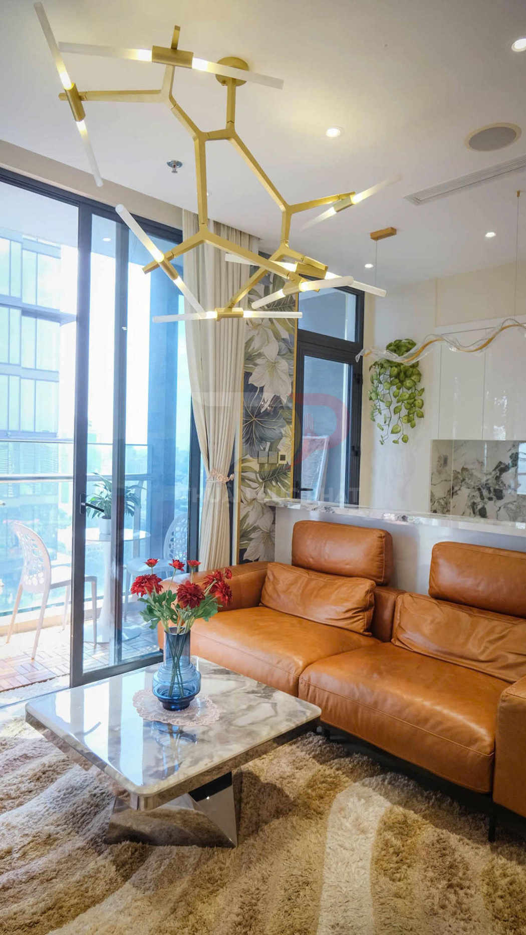 Đèn trần hiện đại khung kim loại vàng treo trên phòng khách với sofa da nâu và bàn đá sang trọng