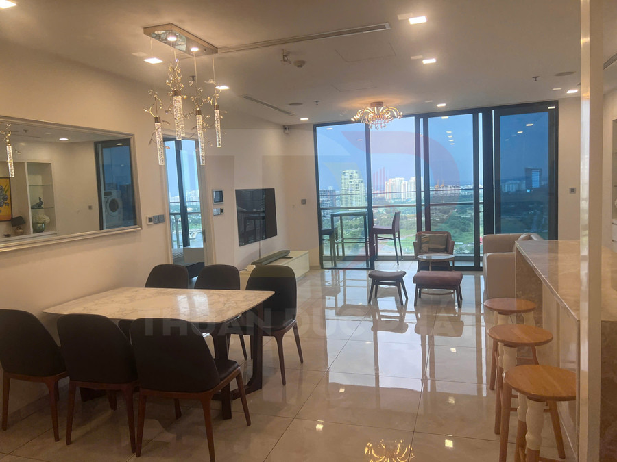 Phòng khách và bếp căn hộ cao cấp với bàn ăn đá, quầy bar, ghế gỗ và cửa kính lớn nhìn ra thành phố