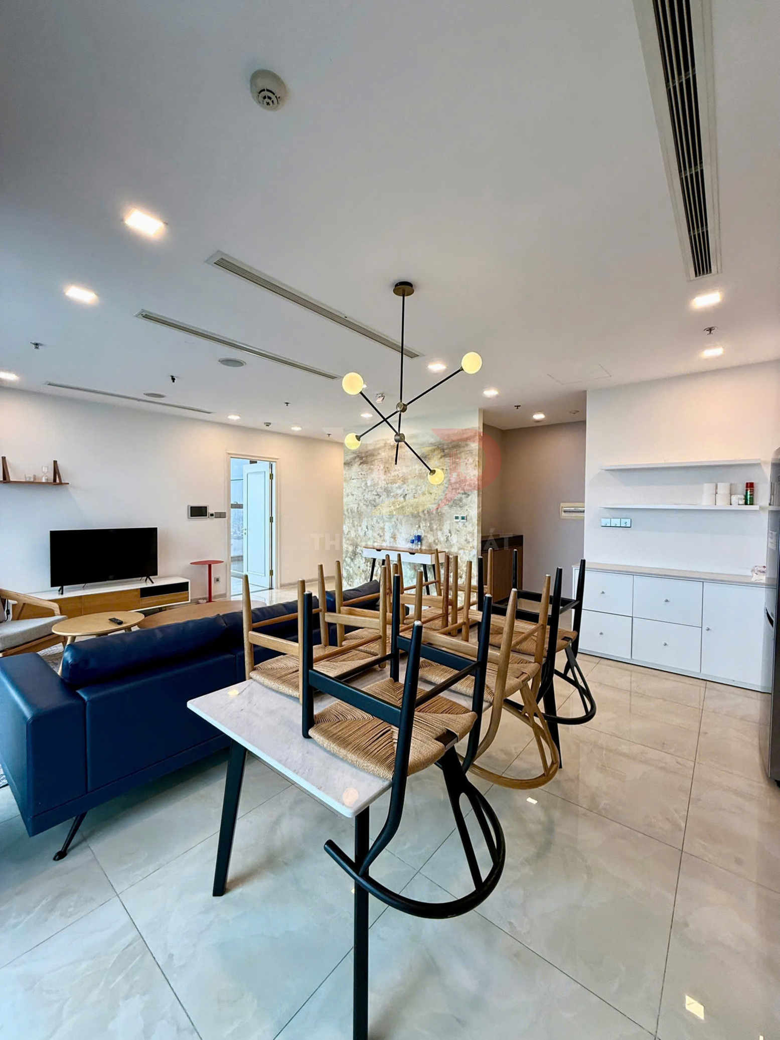 Bàn ăn đá với ghế gỗ lật úp trong phòng khách hiện đại có sofa da xanh và đèn trần trang trí