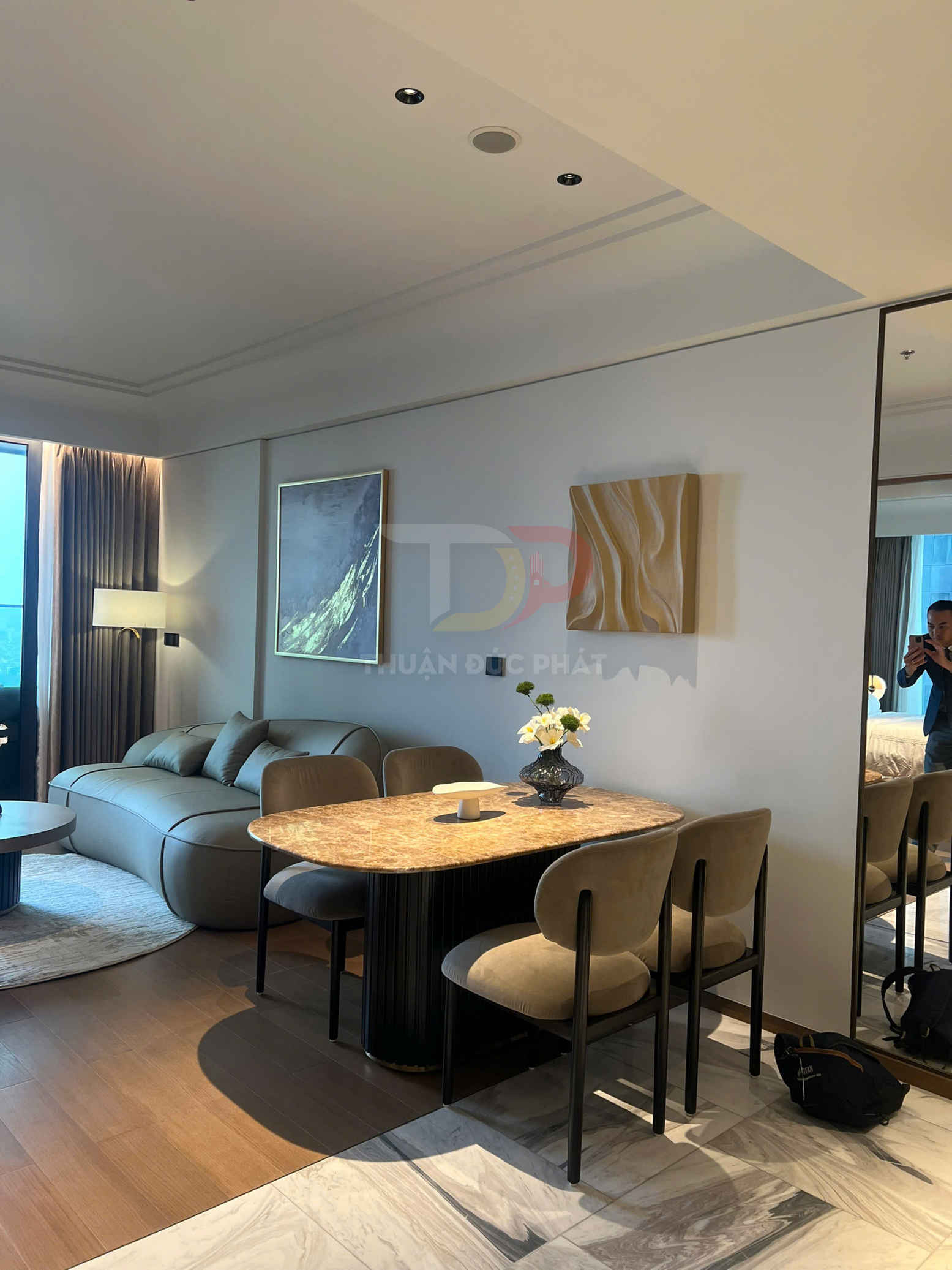 Bàn ăn mặt đá và ghế bọc nỉ trong phòng khách chung cư hiện đại, cạnh sofa và tranh treo tường
