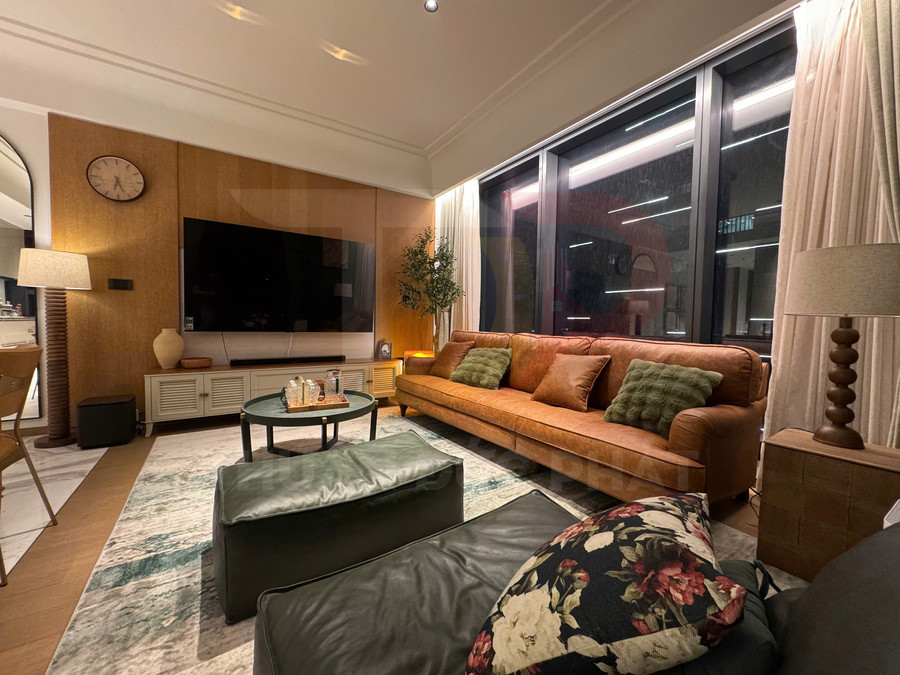 Phòng khách hiện đại với sofa da nâu, bàn trà tròn, tivi màn hình phẳng lớn và đèn trang trí ấm áp