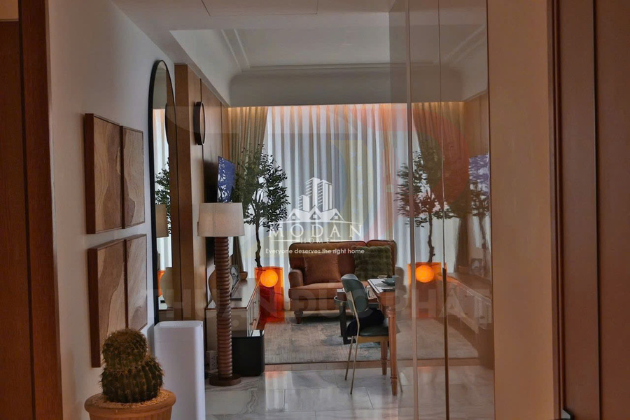 Phòng khách chung cư hiện đại với sofa nâu, bàn trà, đèn trang trí và cây xanh cạnh rèm cửa lớn