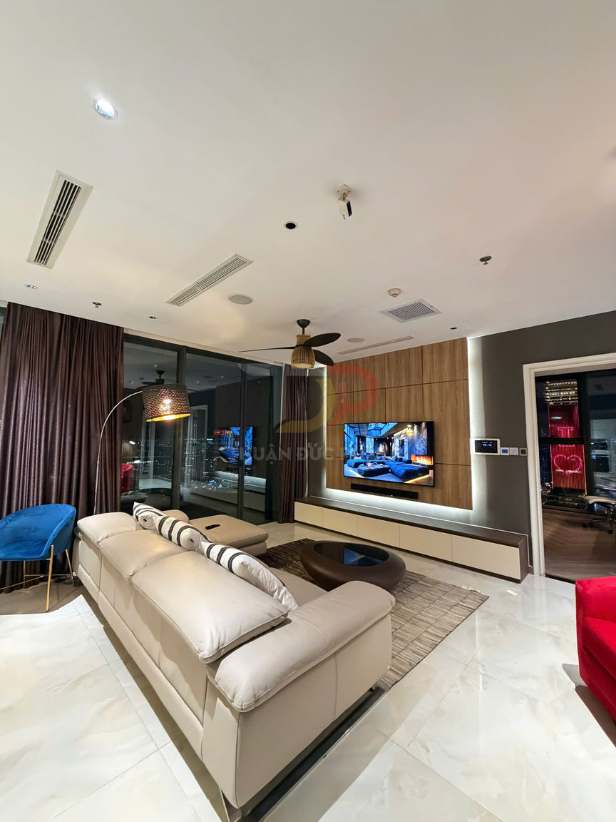 Phòng khách hiện đại với sofa da màu kem, ghế bành xanh, tivi treo tường và bàn trà gỗ trên nền gạch bóng