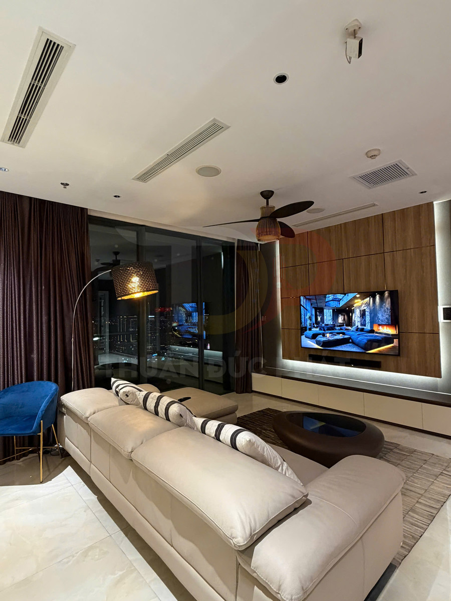 Phòng khách hiện đại với sofa da màu kem, ghế nhung xanh và tivi treo tường cạnh cửa kính lớn