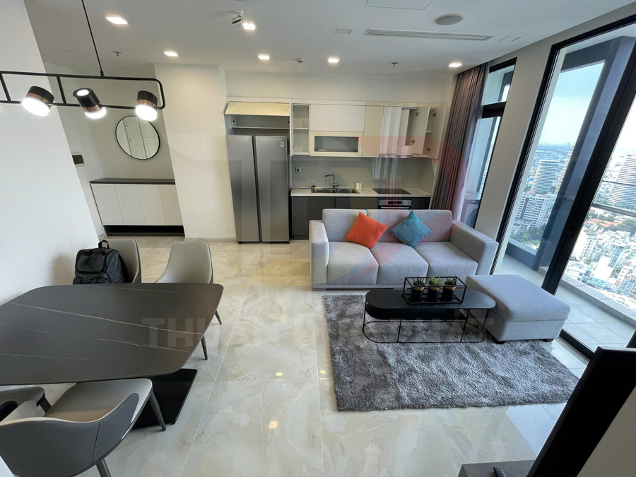 Căn hộ chung cư hiện đại với bếp, sofa xám gối màu, bàn ăn và cửa kính lớn nhìn ra thành phố