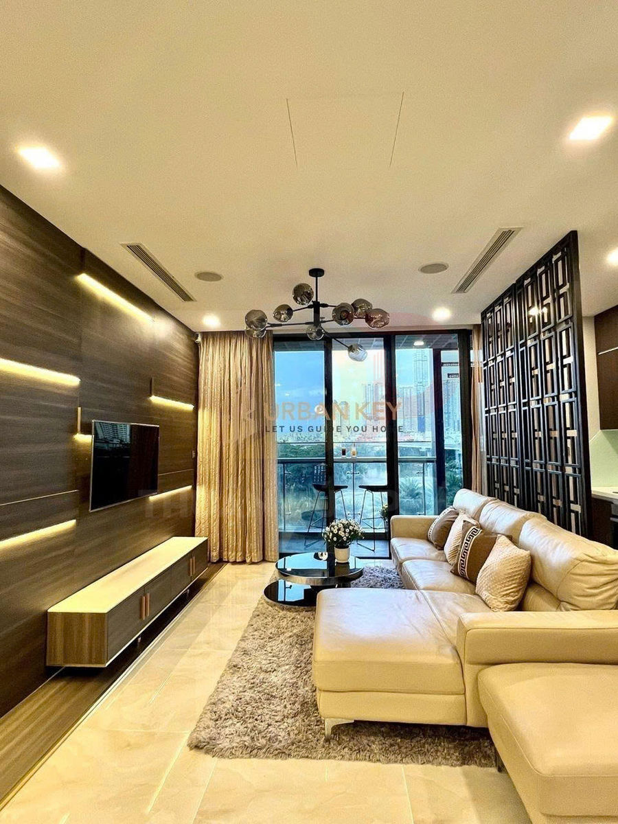 Phòng khách chung cư hiện đại với sofa da chữ L màu kem, bàn trà tròn và tivi treo tường đối diện ban công kính