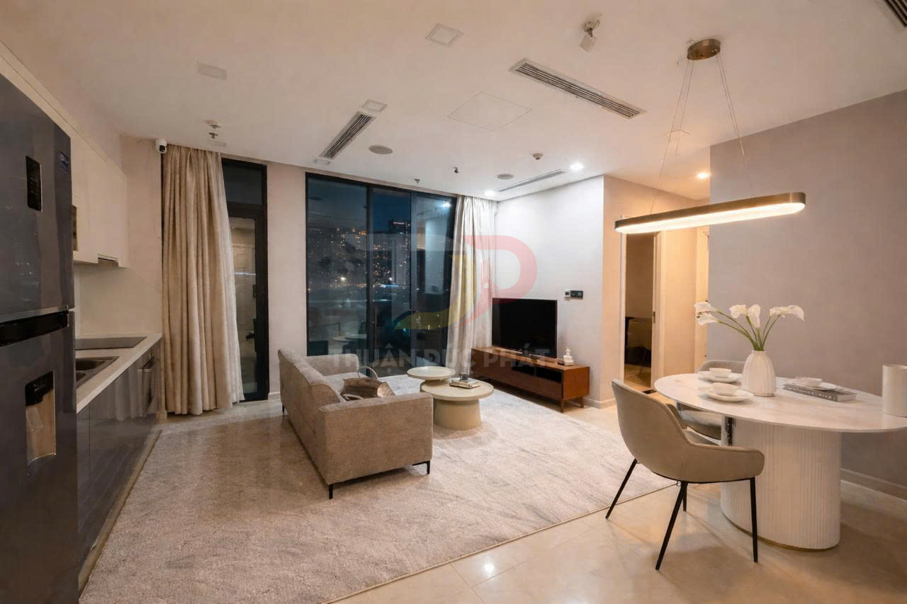Phòng khách căn hộ hiện đại với sofa xám, bàn trà tròn, tivi màn hình phẳng và bàn ăn tròn cạnh bếp