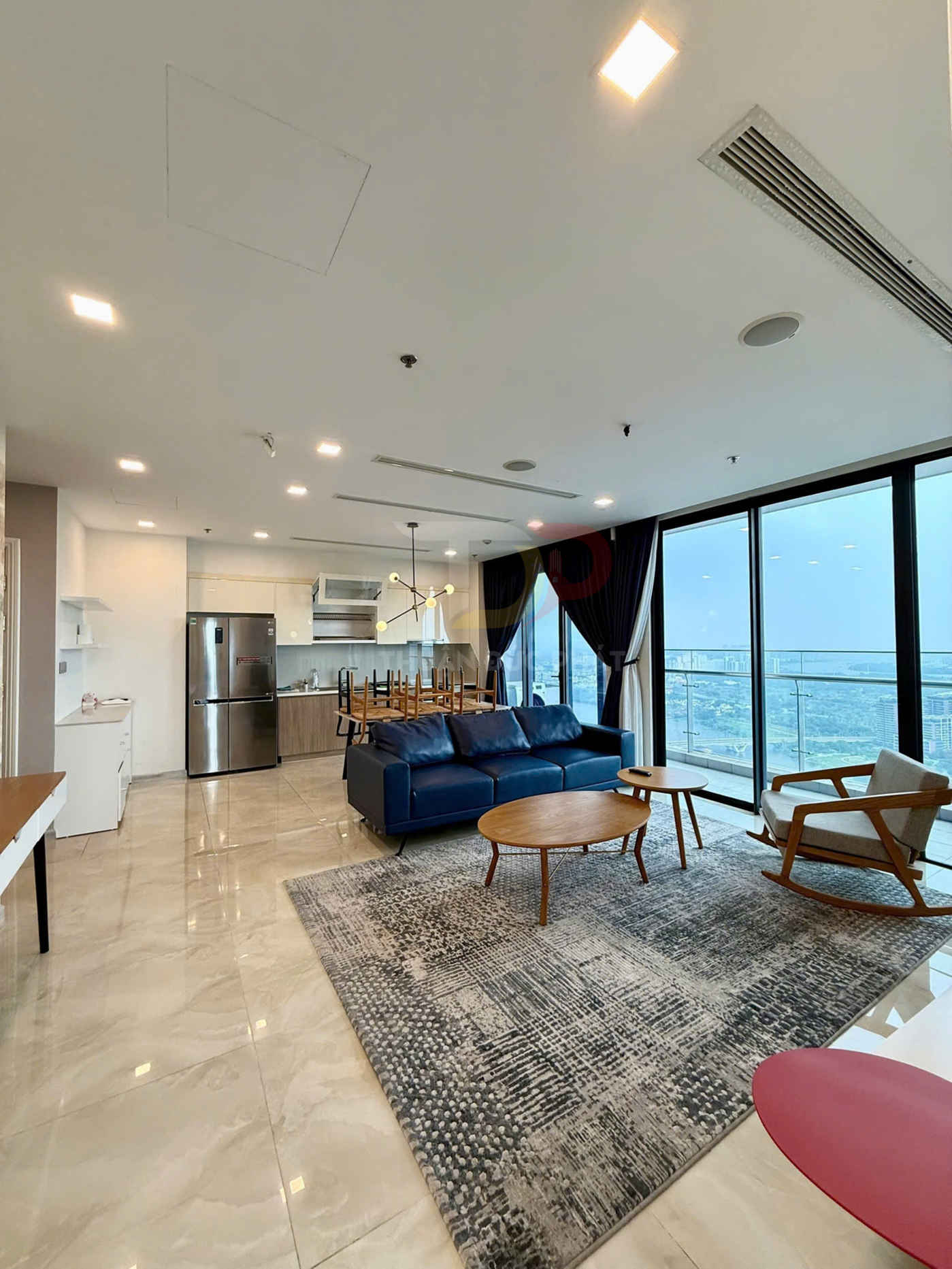 Phòng khách căn hộ hiện đại với sofa da xanh, bàn trà gỗ tròn và cửa kính lớn nhìn ra ban công